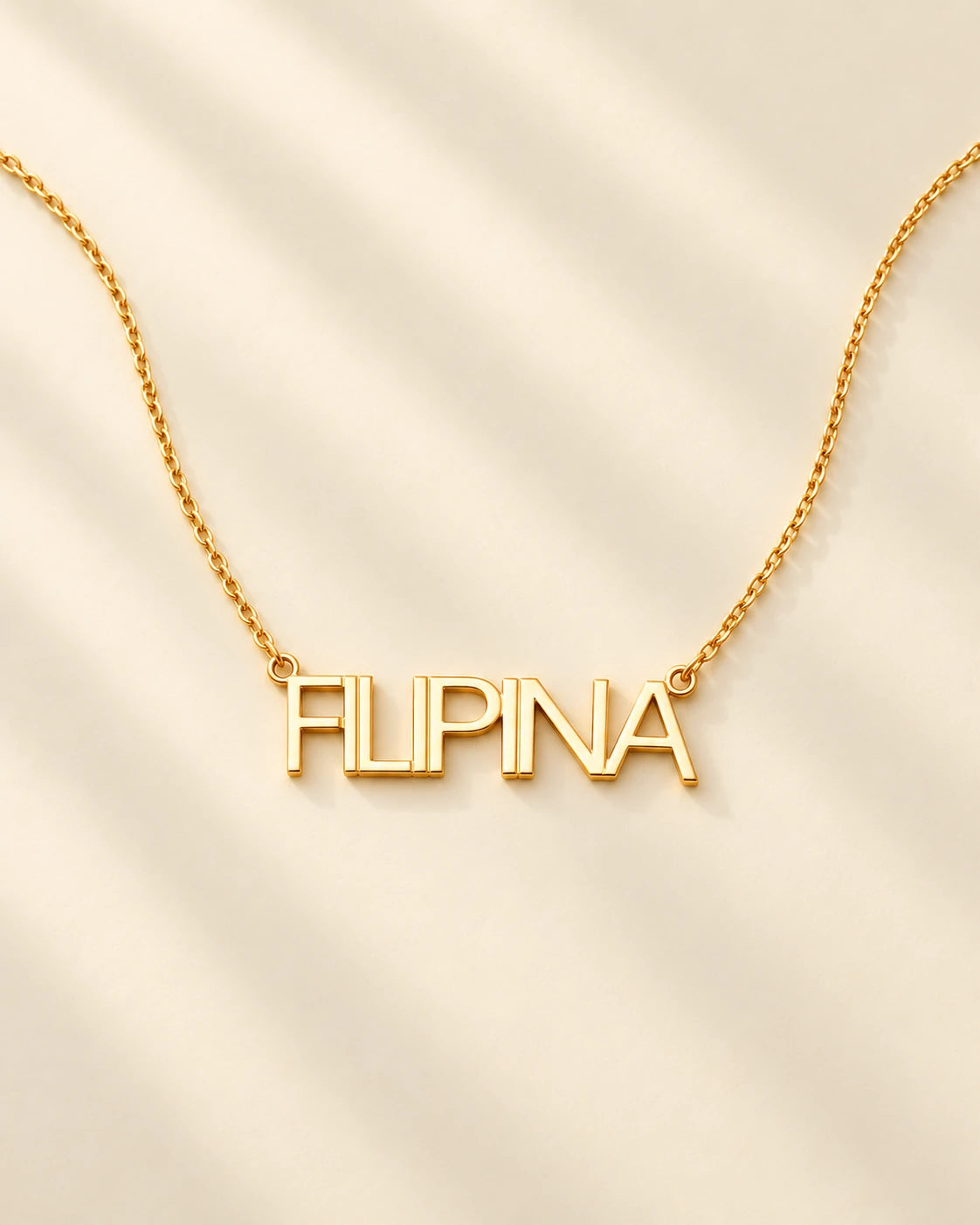 FLEURENZ FILIPINA uppercase 14k gold-filled nameplate necklace on an ivory background