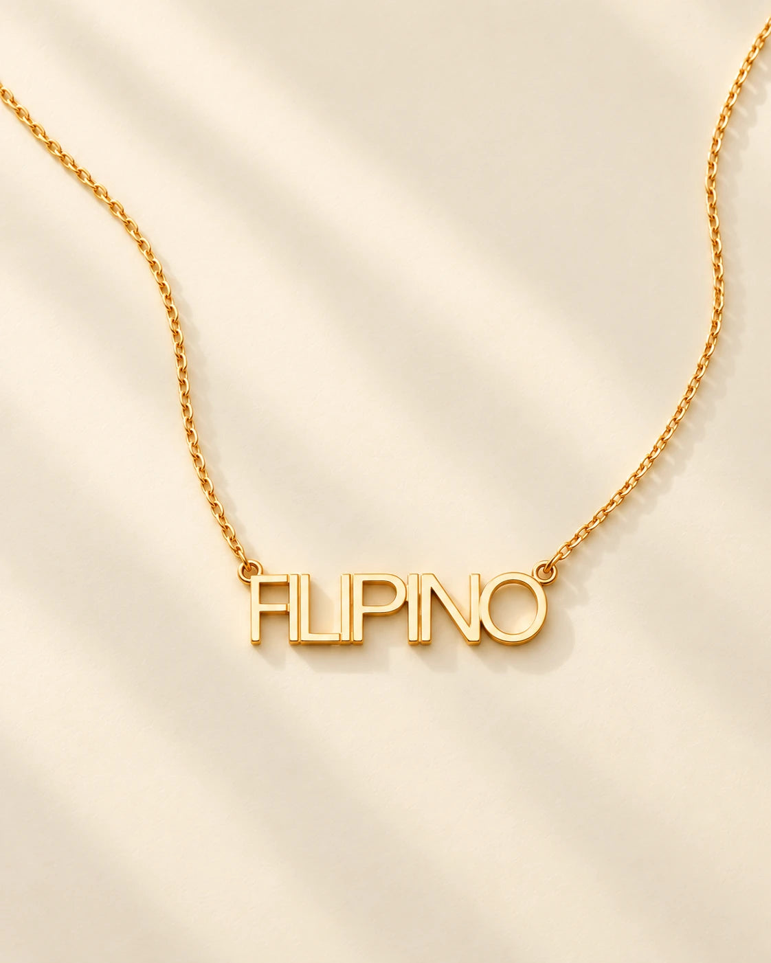FLEURENZ FILIPINO uppercase 14k gold-filled nameplate necklace on an ivory background